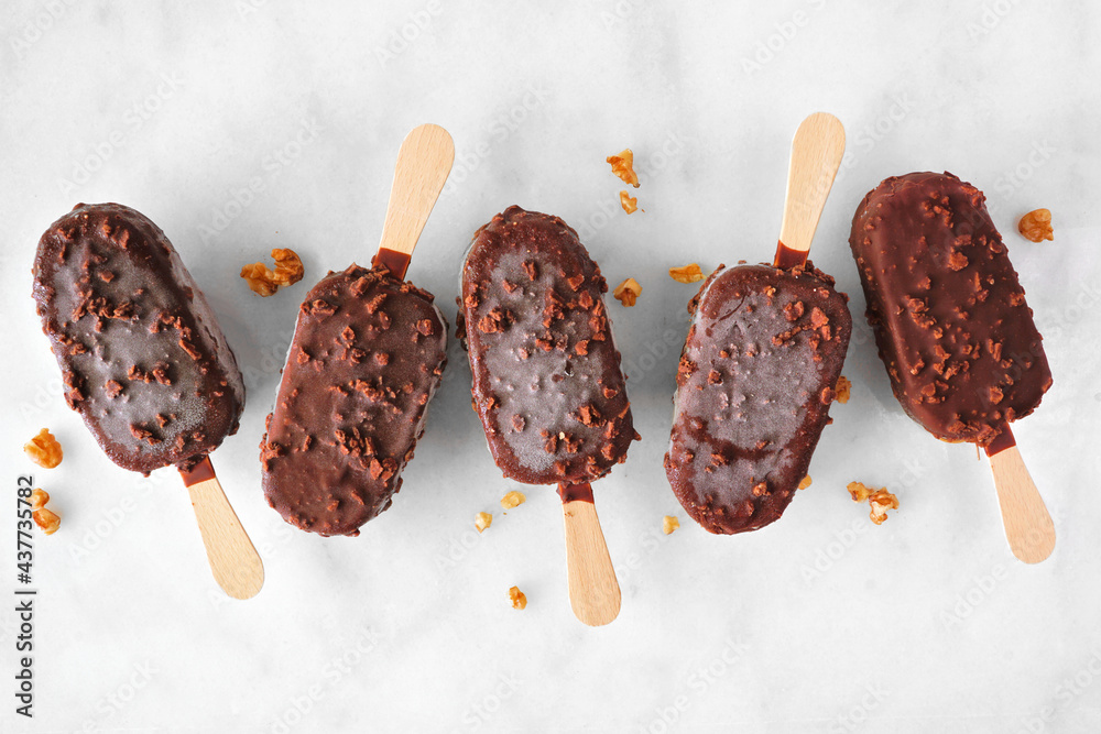Aufkleber chocolate dipped ice cream pops with nuts. top view scattered on white marble background.