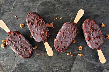 Chocolate dipped ice cream bars with nuts. Overhead view scattered on dark slate background.