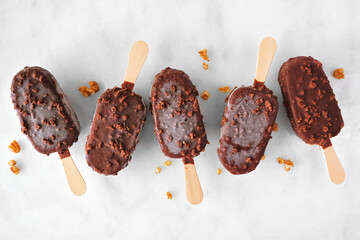 Chocolate dipped ice cream pops with nuts. Top view scattered on white marble background.