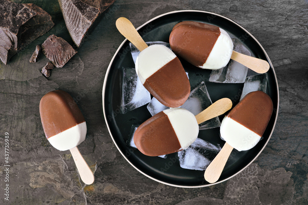 Poster plate of chocolate dipped vanilla ice cream bars. top view over a dark slate background.