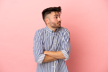 Young caucasian man isolated on pink background making doubts gesture while lifting the shoulders