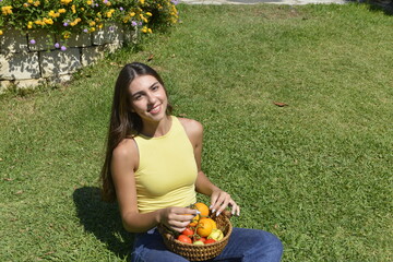 Young women sitting on grass. Girl holding a fruit basket. Happy girl smiling and looking at the camera