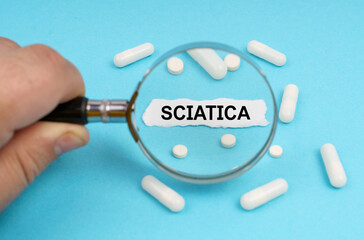 A man looks through a magnifying glass at pills and a leaf with the inscription - SCIATICA