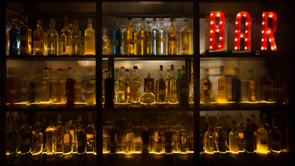 BAR sign with lights in the dark with bottles of alcohol and empty tabletop.  - obrazy, fototapety, plakaty