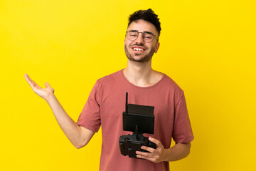 Man holding a drone remote control isolated on yellow background extending hands to the side for inviting to come