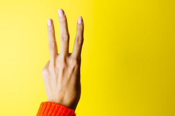 Woman's hand in red sweater shows three with fingers on yellow background