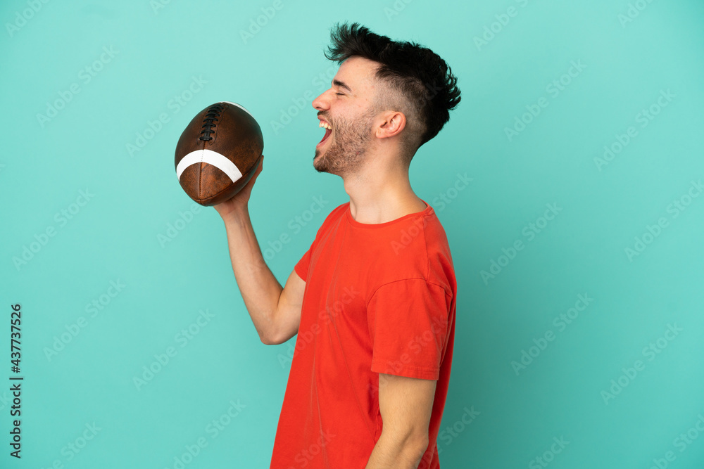 Wall mural Young Caucasian man playing rugby isolated on blue background laughing in lateral position