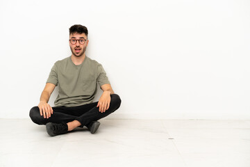 Young caucasian man sitting on the floor isolated on white background with surprise facial expression