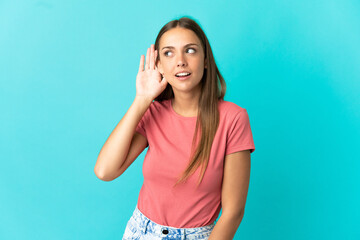 Young woman over isolated blue background listening to something by putting hand on the ear