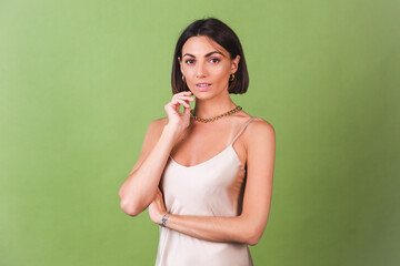 Woman in silk golden dress, huge golden necklace and earrings on green background posing