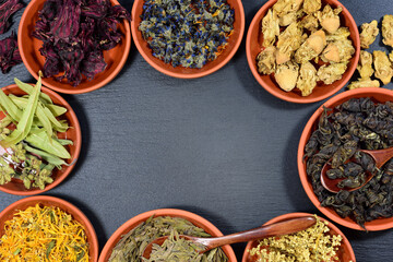 Background and frame made of different clay bowls, in which there are different herbs and teas, with space for text, on a slate plate