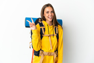 Young mountaineer woman with a big backpack over isolated white background smiling and showing victory sign