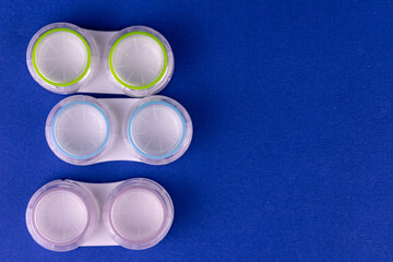 Colored containers for contact lenses for eyes on a blue background.
Copy space.