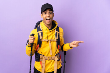 African American man with backpack and trekking poles over isolated background surprised and pointing finger to the side