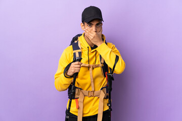 African American man with backpack and trekking poles over isolated background covering mouth with hand