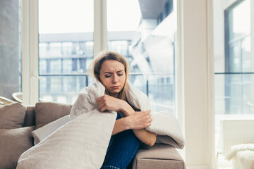 Portrait young woman sitting on sofa at home depressed. Girl is having a hard time with stress. Caucasian female indoors alone worried about problems. unhappy blonde student in living room or bedroom
