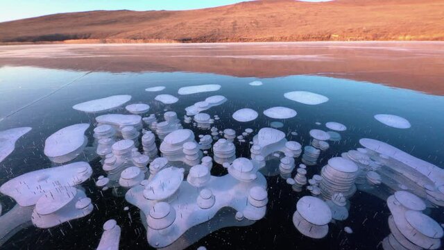 Bubble in ice of frozen lake Baikal. Layered circle pattern surface. Sky and hill reflection
