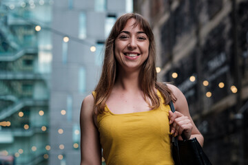 Portrait of a young woman in front of a building with bokeh white lights.