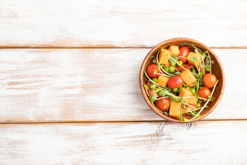 Vegetarian vegetable salad of tomatoes, pumpkin, microgreen pea sprouts on white wooden background. Top view, copy space.