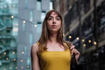 Portrait of a young woman in front of a building with bokeh white lights.