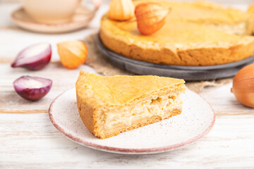 Autumn onion pie and cup of coffee on white wooden background. Side view, selective focus.