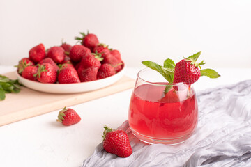 Glass with strawberry lemonade and strawberries on a table with textiles on a white background, summer drinks concept.
