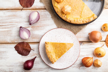 Autumn onion pie decorated with leaves  and cup of coffee on white wooden background. Top view.