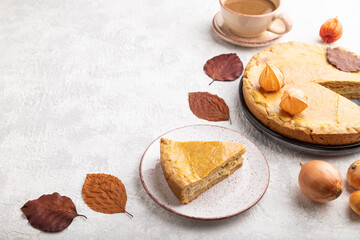 Autumn onion pie decorated with leaves and cup of coffee on gray concrete background. Side view, copy space.