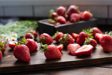 Ripe strawberries on a wooden cutting board in the kitchen with a bouquet of daisies, summer concept.