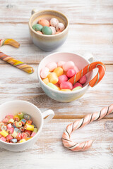 Heap of multicolored caramel candies in cups on white wooden background. side view.