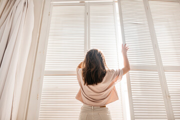 Fototapeta na wymiar morning young girl at the hotel window, white blinds, sunlight