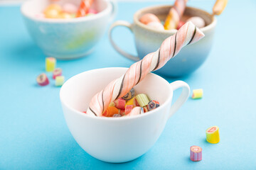 Heap of multicolored caramel candies in cups on blue background. side view, selective focus.