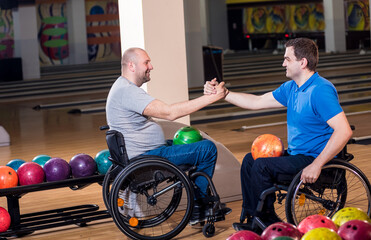 Two young disabled men in wheelchairs playing bowling in the club