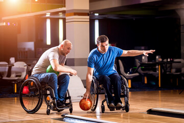 Fototapeta na wymiar Two young disabled men in wheelchairs playing bowling in the club