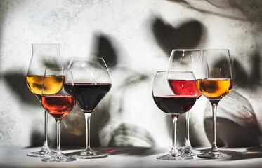 Wines assortment. Red, white, rose wine in wineglasses on gray background. Wine tasting concept. Hard sunlight and shadows from foliage