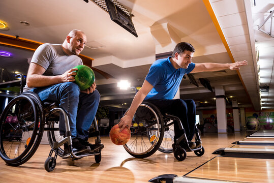 Two young disabled men in wheelchairs playing bowling in the club