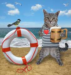 A gray cat sailor in a shirt with a wooden mug of beer stands near a lifebuoy by the sea.