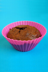 Close-up of homemade gluten-free chocolate muffin with apples in pink silicone mold on blue background. side view