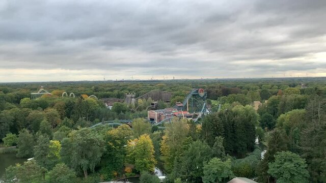 Aerial (drone) footage of Efteling amusement park attractions and rollercoasters surrounded by forest with windmills in the background. Kaatsheuvel, North Brabant,  Netherlands