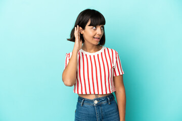 Young mixed race woman isolated on blue background listening to something by putting hand on the ear