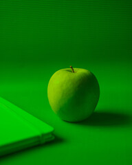 Minimalistic image of green apple on a green background and a green notebook
