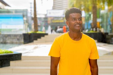 Portrait of handsome black African man wearing yellow t-shirt outdoors in city during summer