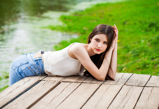 Young beautiful brunette girl in posing against the background of a pond in a summer park