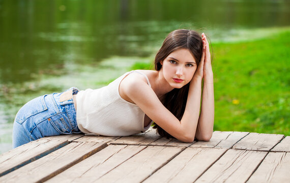 Young beautiful brunette girl in posing against the background of a pond in a summer park