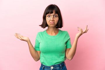 Young mixed race woman isolated on pink background having doubts while raising hands