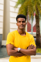 Obraz premium Portrait of handsome black African man wearing yellow t-shirt outdoors in city during summer with arms crossed