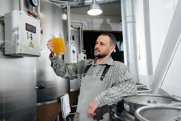 A young bearded brewer conducts quality control of freshly brewed beer in the brewery.