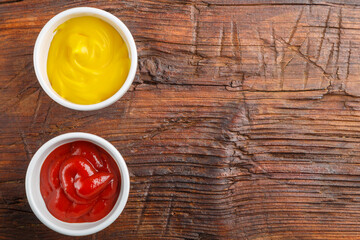 Sauce boats with cheese sauce and ketchup on a wooden table. Save a place.