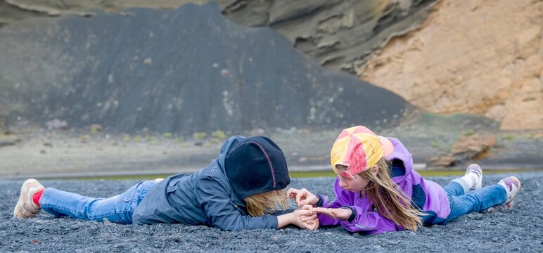2 kleine M&auml;dchen untersuchen in Bauchlage das Lavagestein am Lago Verde auf Lanzarote