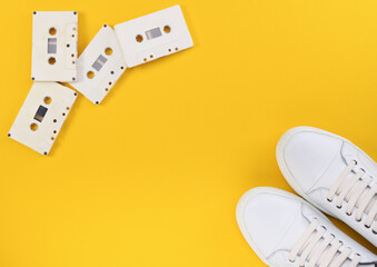Vintage audio cassettes in white and white sneakers on a yellow background. Music listening...